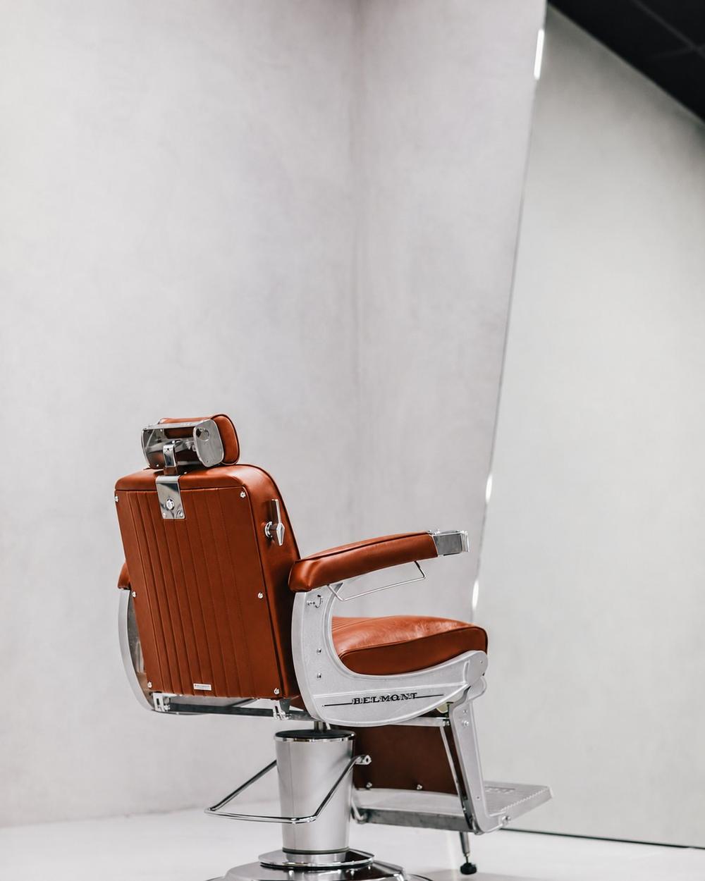 Burnt orange Belmont barber chair beside large leaning mirror in minimalist studio interior